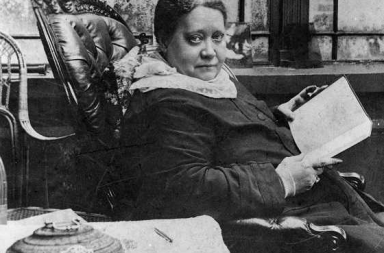 Helena Blavatsky sentada com um livro aberto.