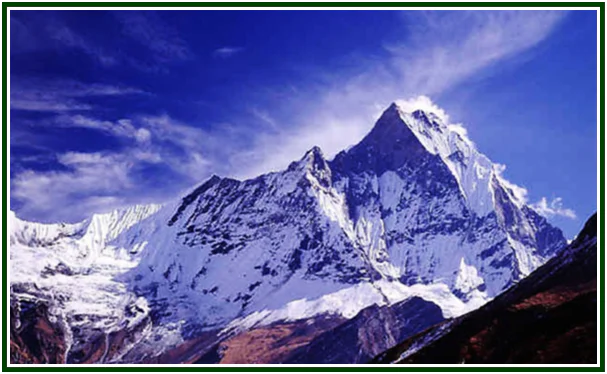 A majestic view of the snow-capped Machapuchare mountain peak in the Himalayas under a blue sky with scattered clouds.