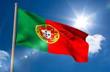 Bandeira de Portugal a ondular ao vento sob um céu claro, ilustrando a meditação prática 'Oração Pelo Despertar de Portugal' de Carlos Cardoso Aveline.
