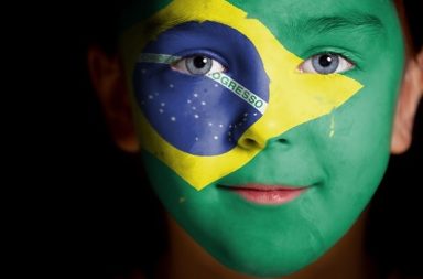 Fotografia de uma criança sorridente com a bandeira do Brasil pintada no rosto, simbolizando a esperança no futuro.