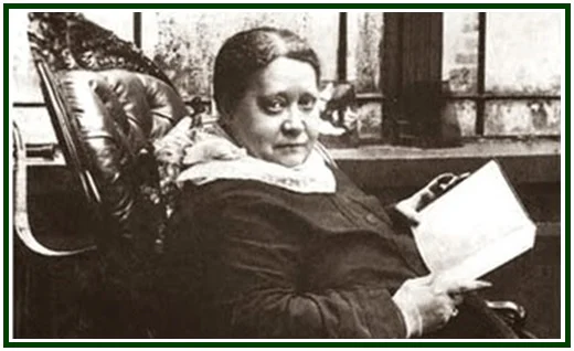 Helena Blavatsky sentada com um livro aberto.