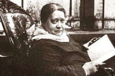 Helena Blavatsky sentada com um livro aberto.