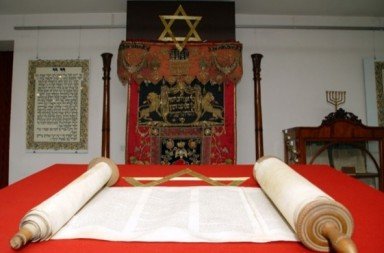 Sagrada Torá judaica aberta sobre mesa vermelha com símbolos esotéricos, associada à lista de tópicos sobre Nazismo e Teosofia.