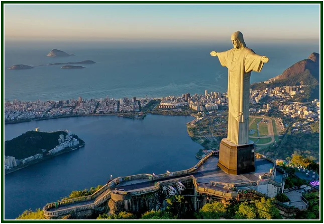 Vista aérea da estátua do Cristo Redentor de braços abertos no topo do Corcovado, com a cidade do Rio de Janeiro e o oceano ao fundo.