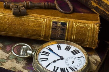 Livros antigos com capa de couro, uma chave de metal e um relógio de bolso antigo sobre a mesa.