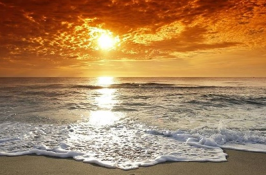 Ondas suaves quebrando na areia com espuma branca sob um céu dourado e ensolarado no oceano, ilustrando A Importância de Saber Parar.