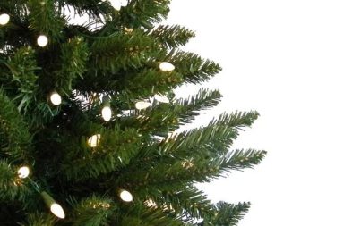Detalhe aproximado dos ramos verdes de uma árvore de Natal decorada com luzes brilhantes, usada para exemplificar a simbologia tradicional.