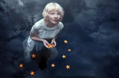 Rapariga na água rodeada de estrelas-do-mar que refletem o cosmos, ilustrando a simetria no ser humano.