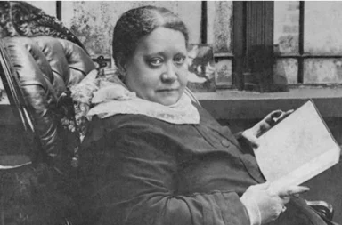 Retrato fotográfico histórico en blanco y negro de HP Blavatsky sentada en un sillón clásico de cuero tallado, sosteniendo un libro abierto mientras mira fijamente hacia adelante, enmarcado por un fino borde verde.