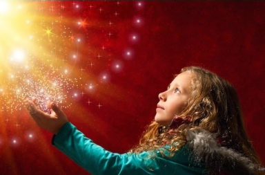 Retrato fotográfico em plano médio de uma menina de perfil com cabelos longos e casaco azul, olhando para cima e estendendo as mãos em direção a uma intensa luz dourada e brilhante com estrelas sobre um fundo vermelho, representando a contemplação do infinito.
