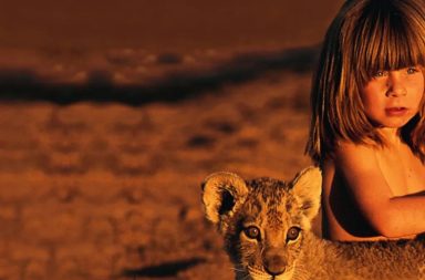 Fotografia da menina Tippi Degre ao lado de um filhote de leão no deserto, ilustrando a sabedoria e a união com a natureza.