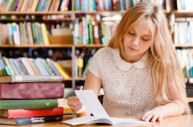 Jovem estudante loura concentrada a ler um documento numa biblioteca com estantes cheias de livros ao fundo, ilustrando o estudo da filosofia esotérica.