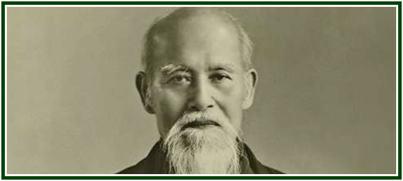 Retrato fotográfico histórico de Morihei Ueshiba, o fundador cujos ensinamentos estabeleceram a filosofia do aikidô, exibindo o seu rosto sereno com uma longa barba e bigode brancos, contra um fundo neutro de estúdio.