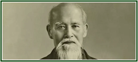 Retrato fotográfico histórico de Morihei Ueshiba, o fundador cujos ensinamentos estabeleceram a filosofia do aikidô, exibindo o seu rosto sereno com uma longa barba e bigode brancos, contra um fundo neutro de estúdio.