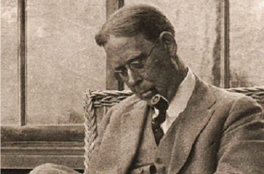Fotografia histórica de John Garrigues, pioneiro da teosofia original, de óculos e fato, sentado a limpar um cachimbo.