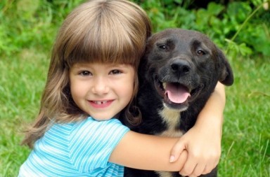 A young girl smiling and hugging a happy dark dog on green grass, illustrating the bond of theosophy and trust.