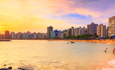 Fotografia de uma praia urbana com prédios ao fundo durante o pôr do sol, ilustrando a jornada de descoberta na teosofia.