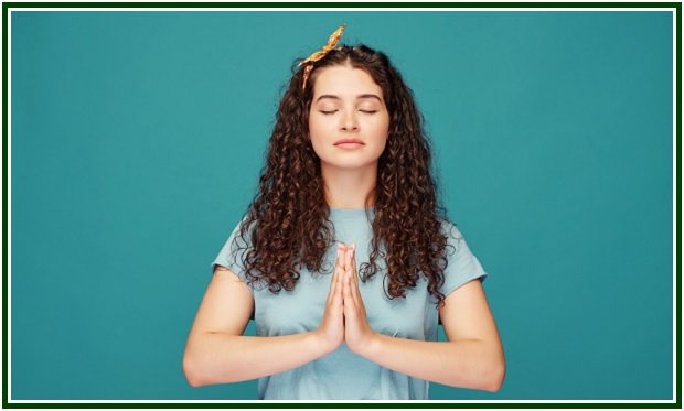 Mulher de olhos fechados fazendo o gesto de namastê com as mãos unidas em meditação, com fundo azul.