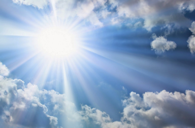 Sol brilhante no céu azul emitindo raios intensos por entre nuvens brancas, ilustrando que a vida é bela.
