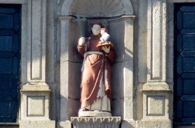 Estátua de Santo António de Lisboa num nicho de pedra, segurando a cruz e o Menino Jesus, inspirando a paz interior.