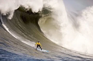 Surfer in a yellow jacket riding a massive big wave at Mavericks representing the science of opportunities and karma.