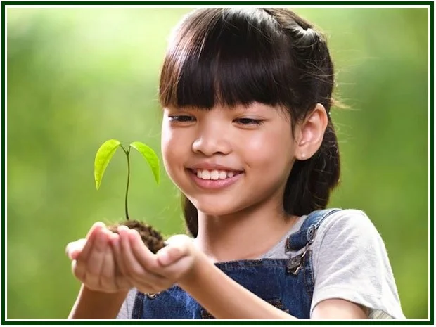 A young girl smiling while holding a small growing plant, symbolizing the moral causes and karma that shape the world state.